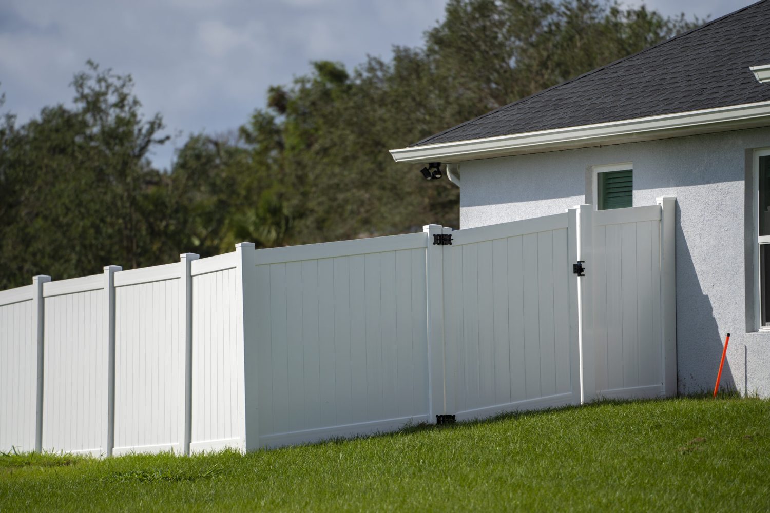 White vinyl picket fence on green lawn surrounding property grounds for backyard protection and privacy.